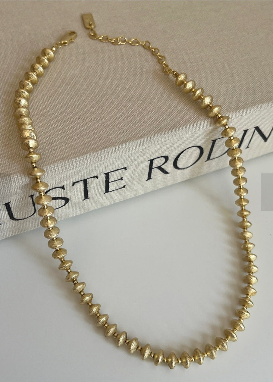 Gold beaded necklace on a beige fabric background