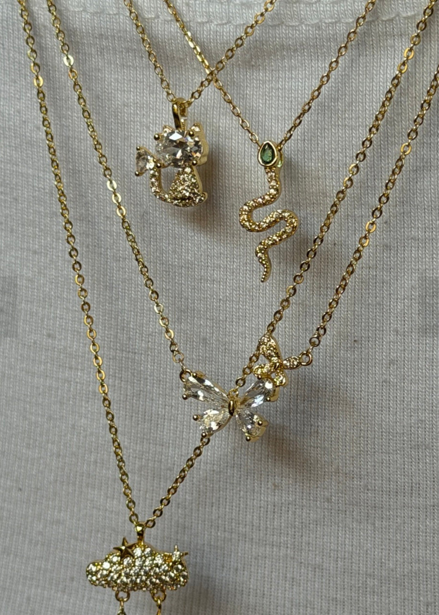 Three gold necklaces with various pendants on a light gray background