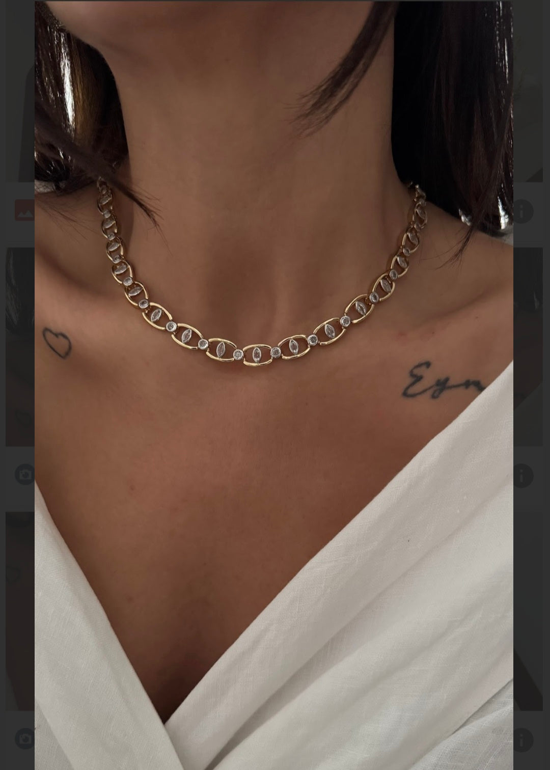 Gold chain necklace worn by a person with a white garment and visible tattoos.