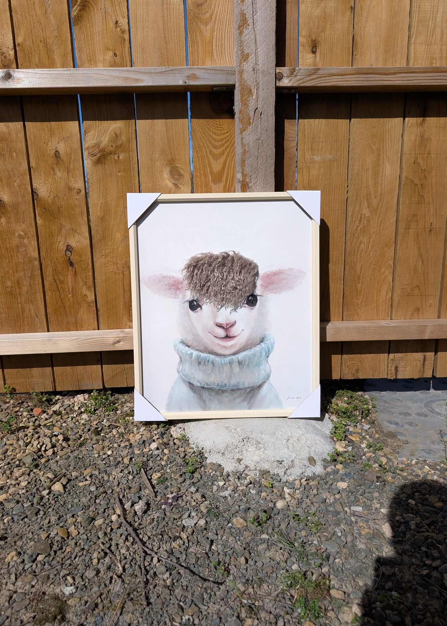 Framed artwork of a fluffy animal in front of a wooden fence