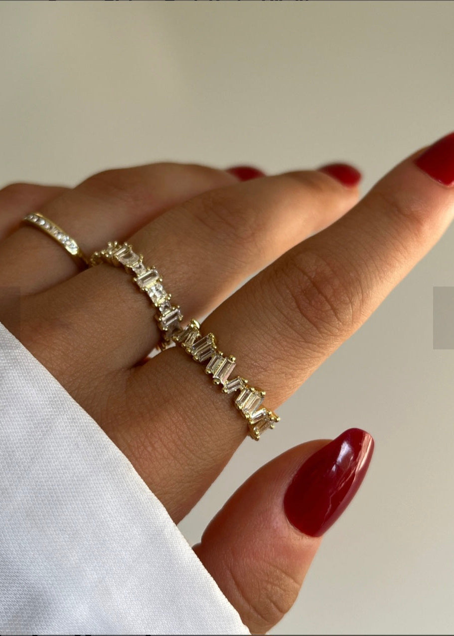 Close-up of a hand wearing two gold rings with gemstones on a neutral background