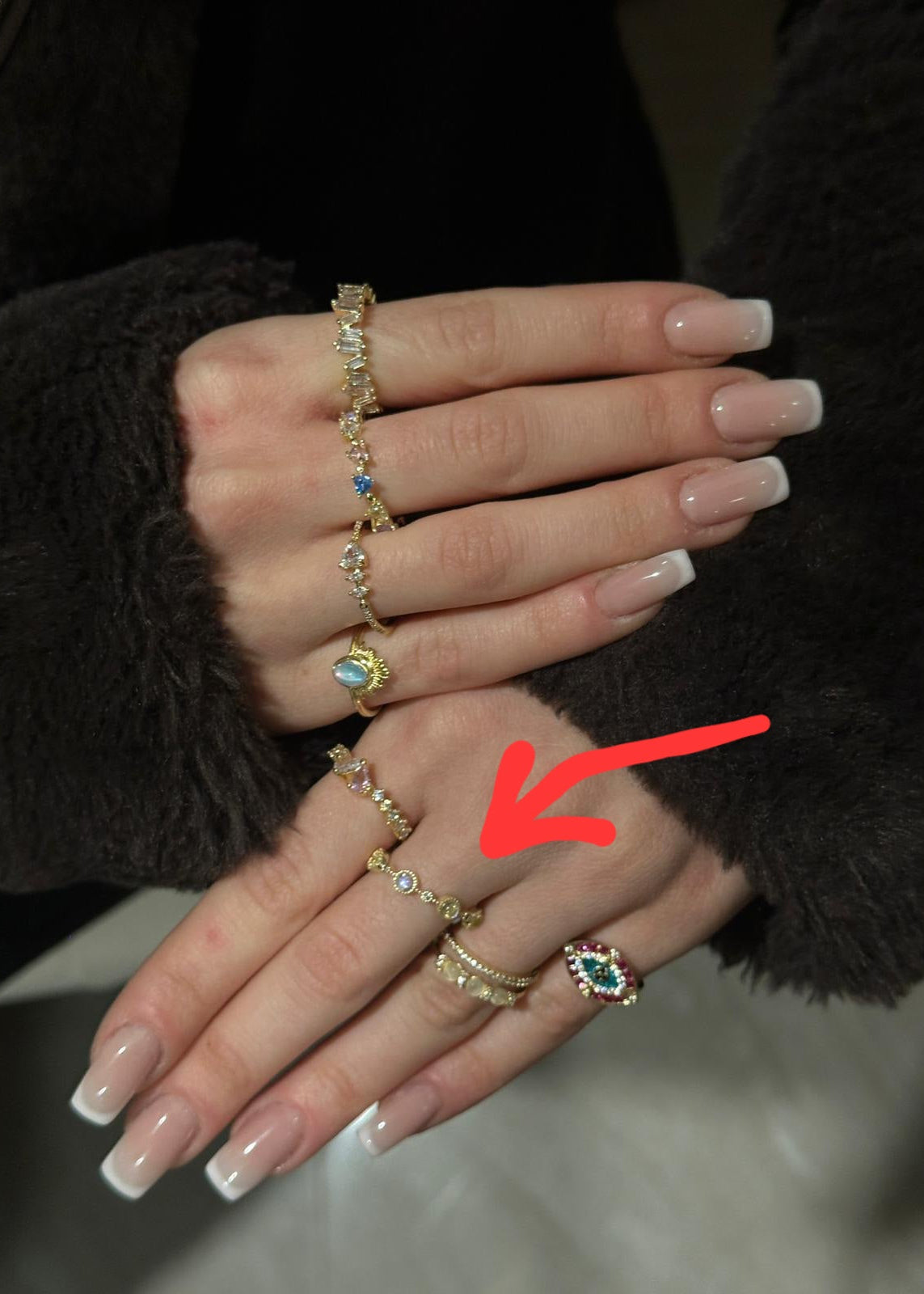 Close-up of a hand wearing multiple gold rings with gemstones, one of which is highlighted by a red arrow.