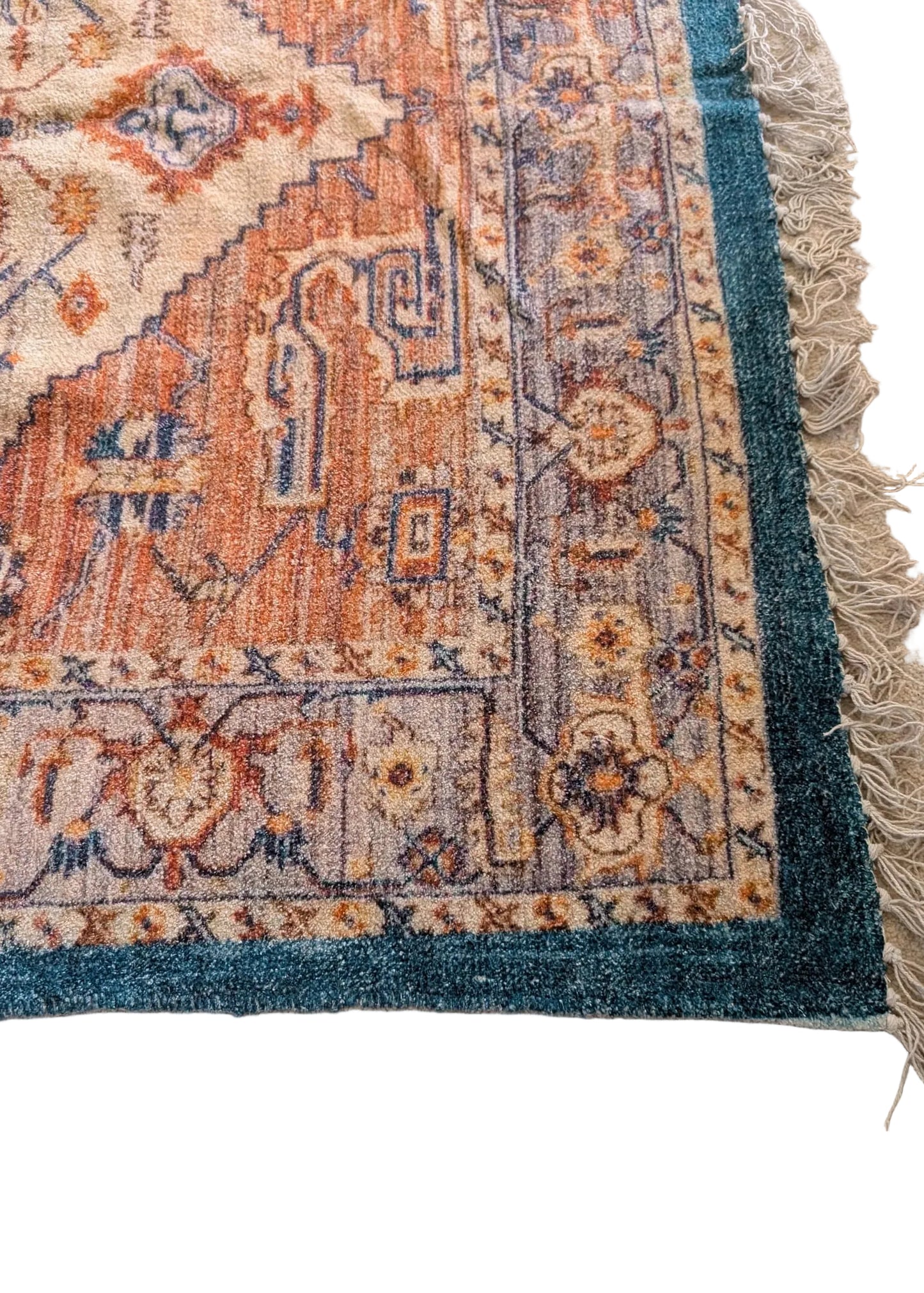 Close-up of a patterned rug corner with intricate designs on a beige floor.