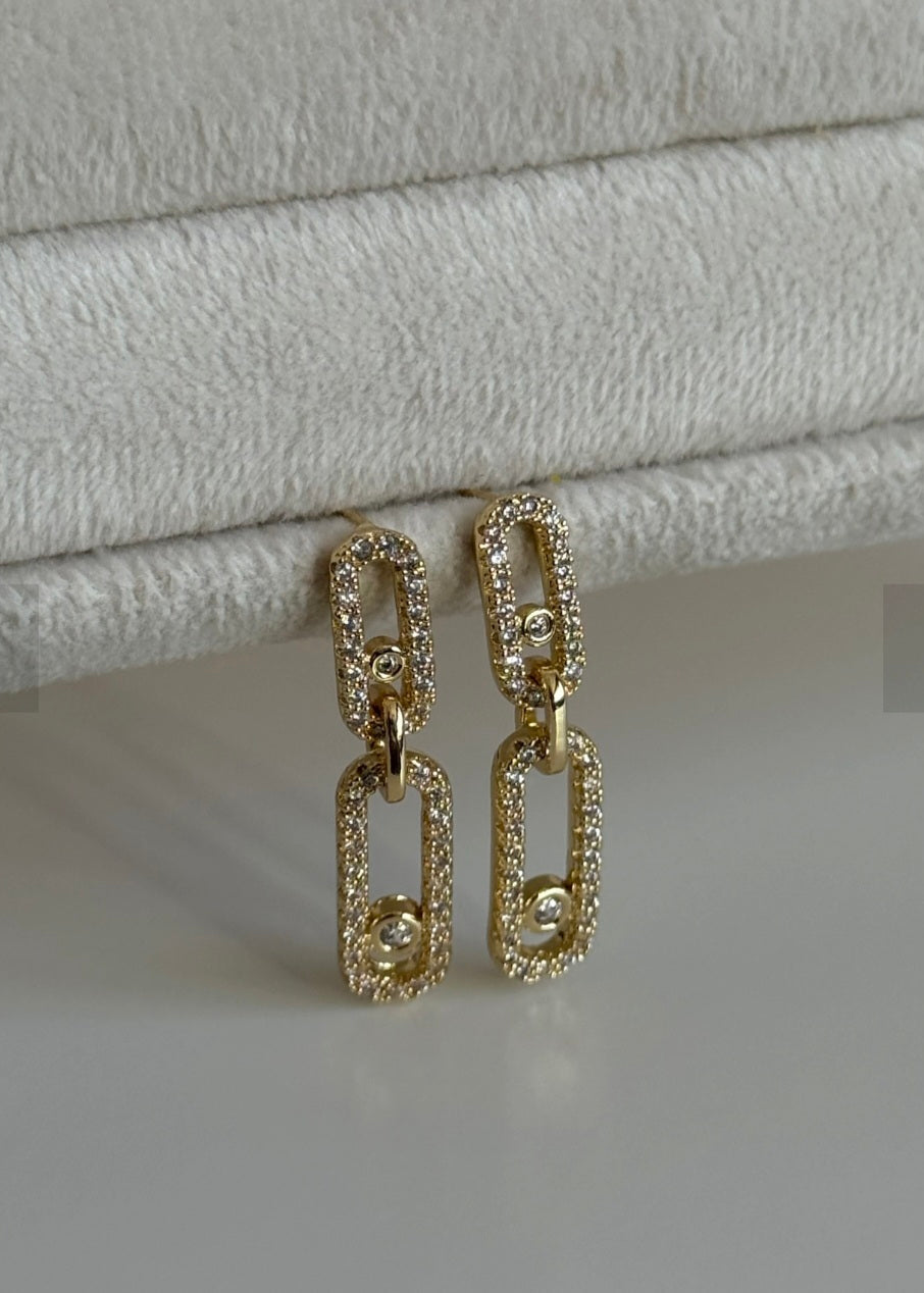 Gold chain earrings on a textured gray surface