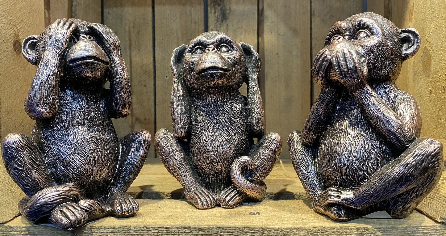 Set of three bronze effect monkey figurines representing see hear speak no evil poses on wooden shelf