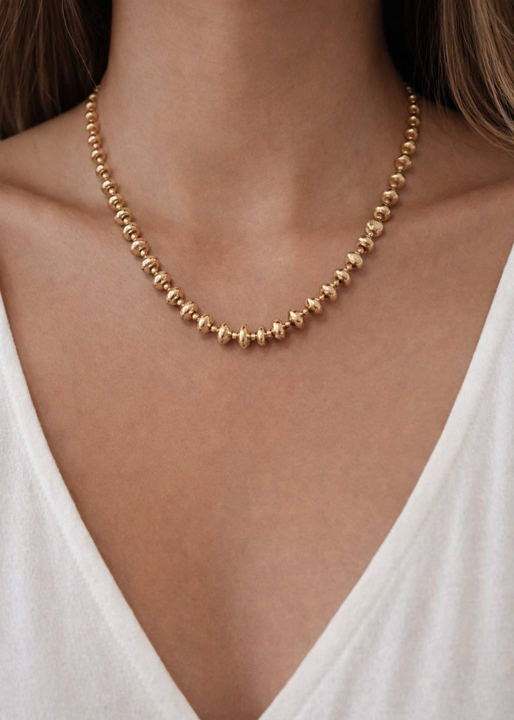 Gold beaded chain necklace with polished round beads worn on neck