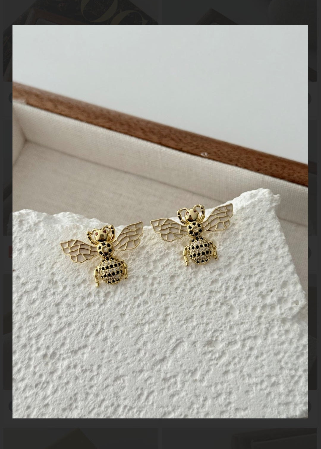 Gold bee stud earrings with zircon stones and detailed wings on textured surface