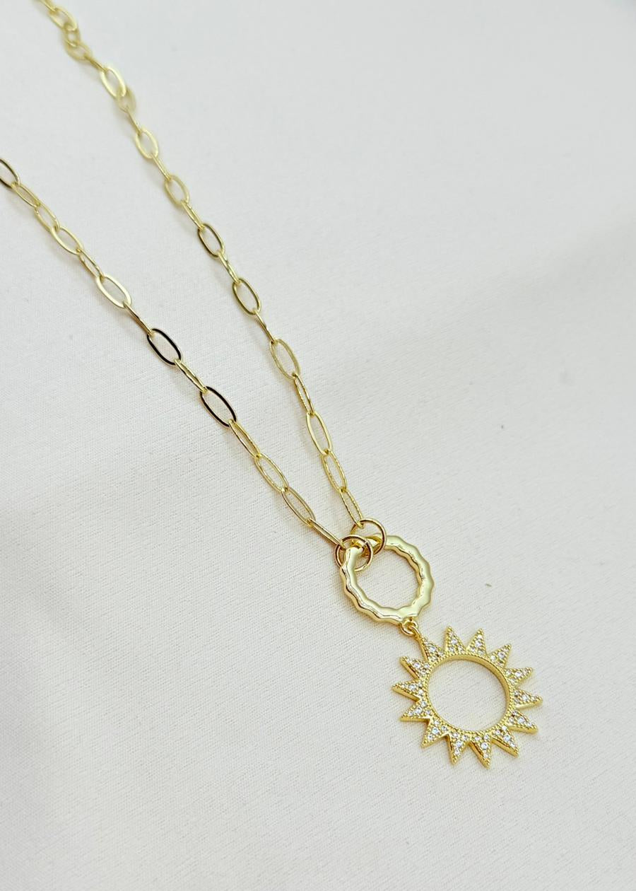 Gold necklace with a sun-shaped pendant on a light gray background