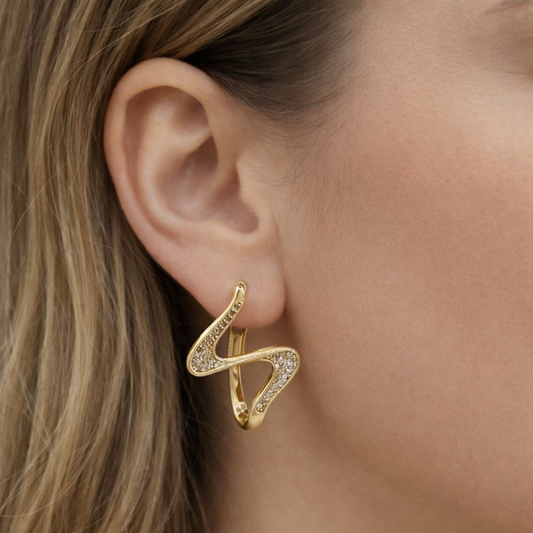 Gold abstract wave statement earrings with sparkling stones worn on ear, modern sculptural jewelry design