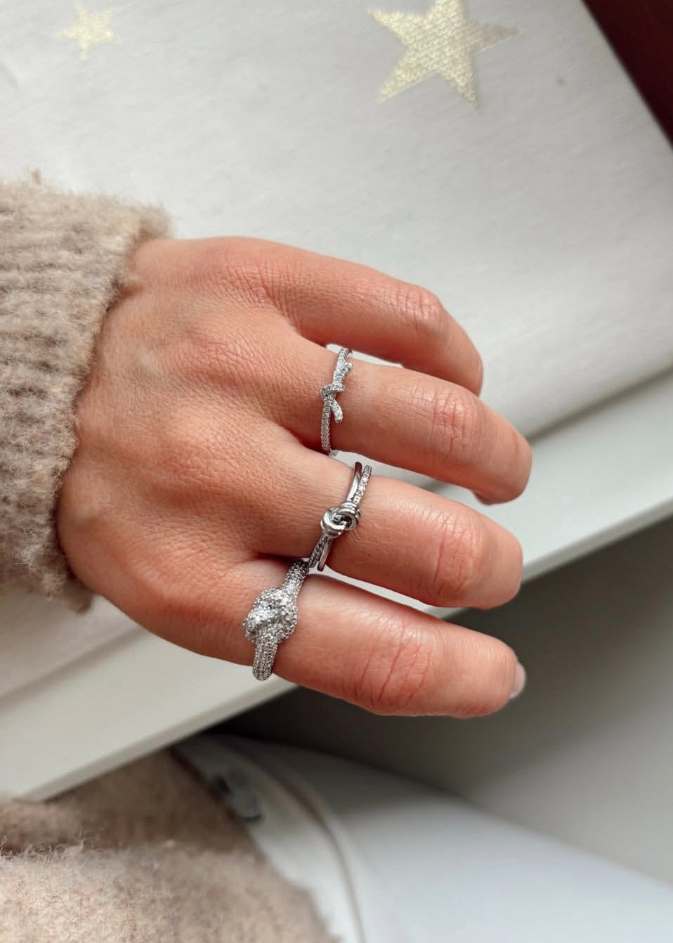 Hand wearing multiple silver rings with a starry background