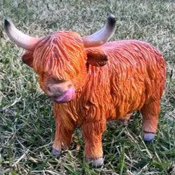 Miniature coloured Highland cow resin figurine with shaggy coat standing on grass