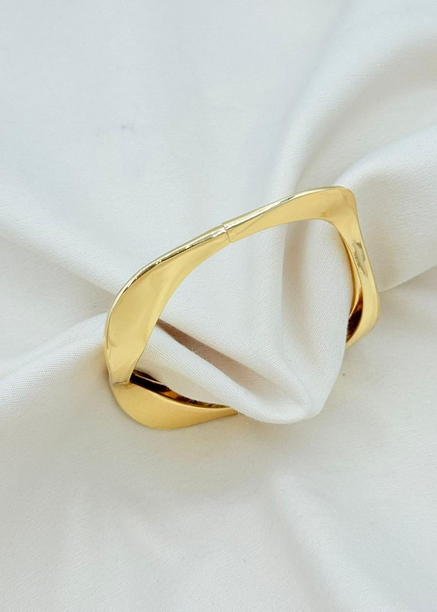 Minimalist sculptural gold cuff bracelet with smooth curved open bangle design on neutral fabric background