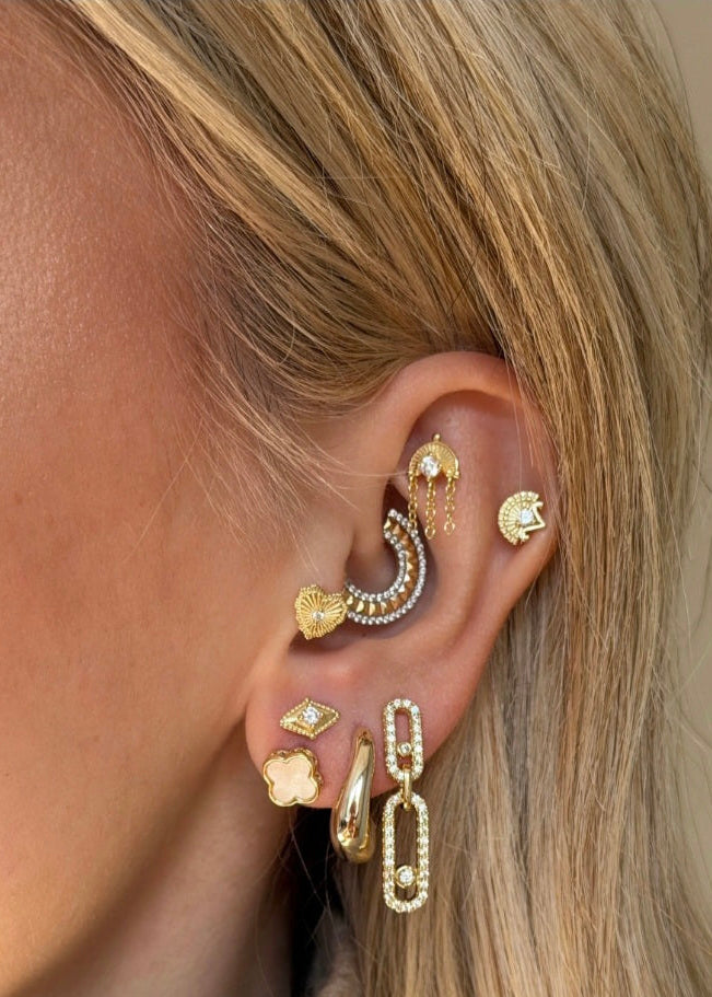 Close-up of an ear with multiple gold earrings on a neutral background