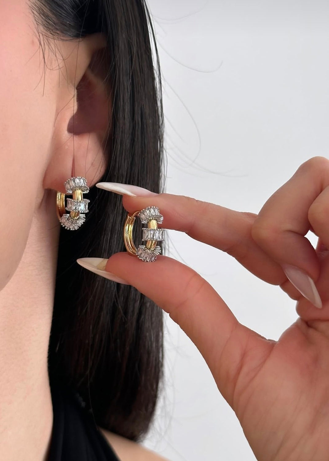 Close-up of a person wearing gold hoop earrings with clear stones.