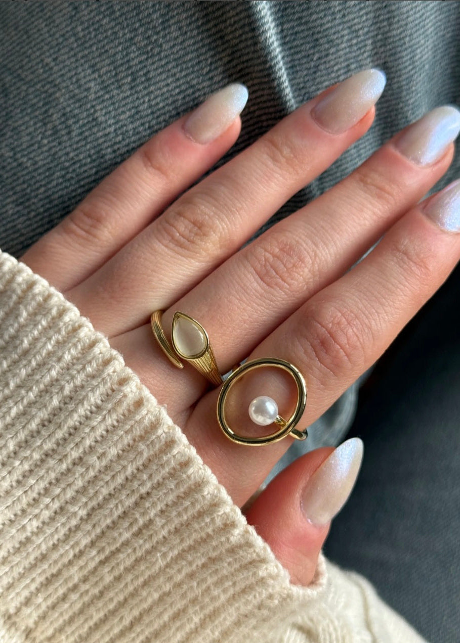 Hand wearing two gold rings with a pearl on a neutral background