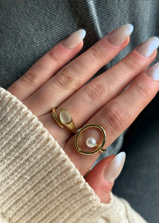 Hand wearing two gold rings with a pearl on a neutral background