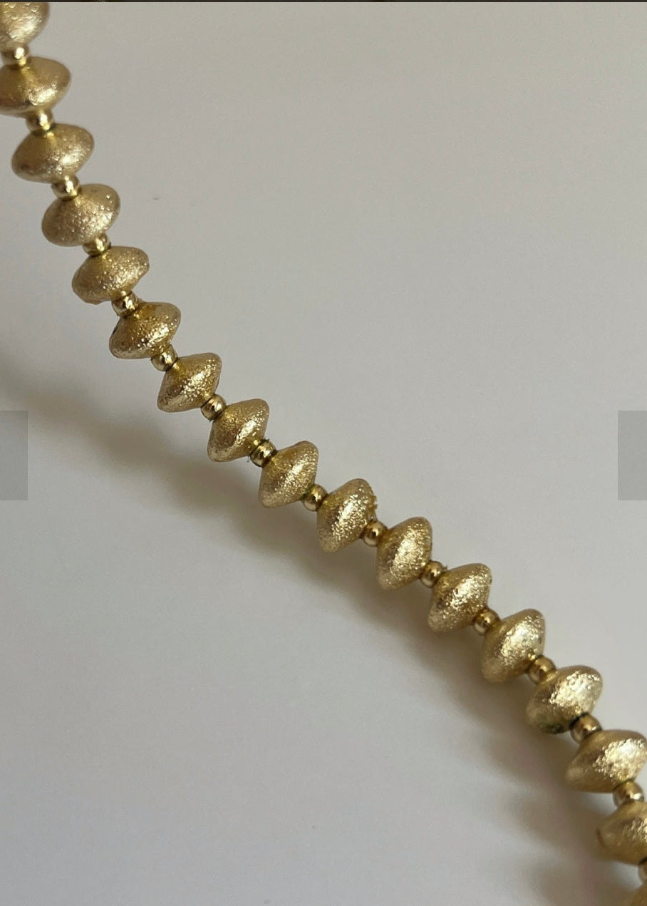 Gold beaded necklace on a light gray background