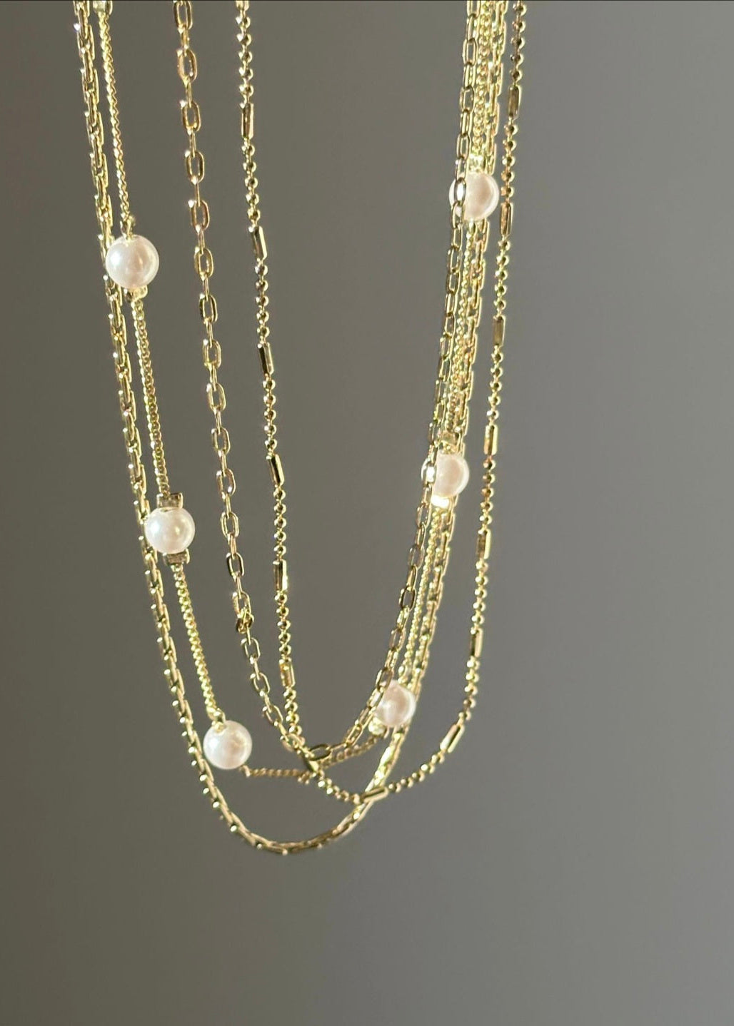 Gold chain necklace with pearl beads on a gray background