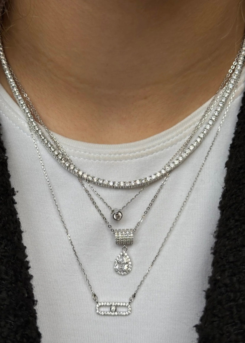 Close-up of a person wearing multiple silver necklaces with a plain background