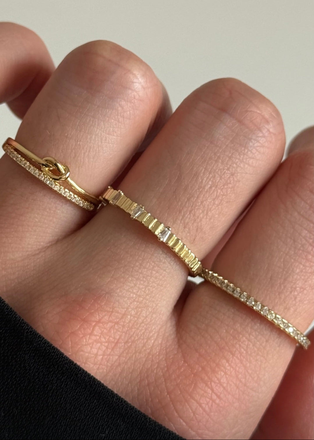 Gold bracelet and ring on a person's wrist with a plain background