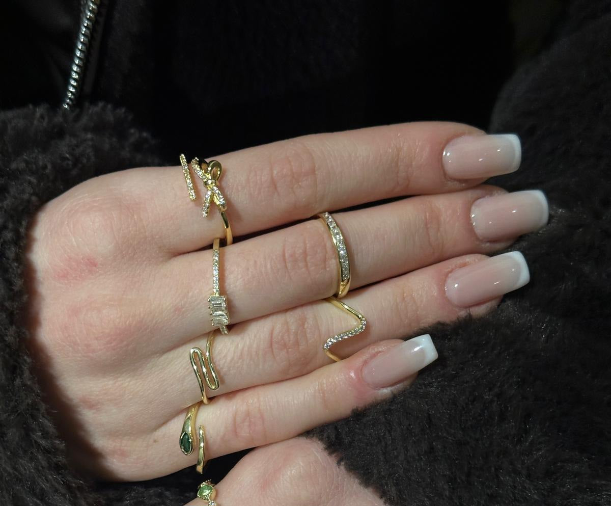 Hand wearing multiple gold rings with gemstones on a dark background