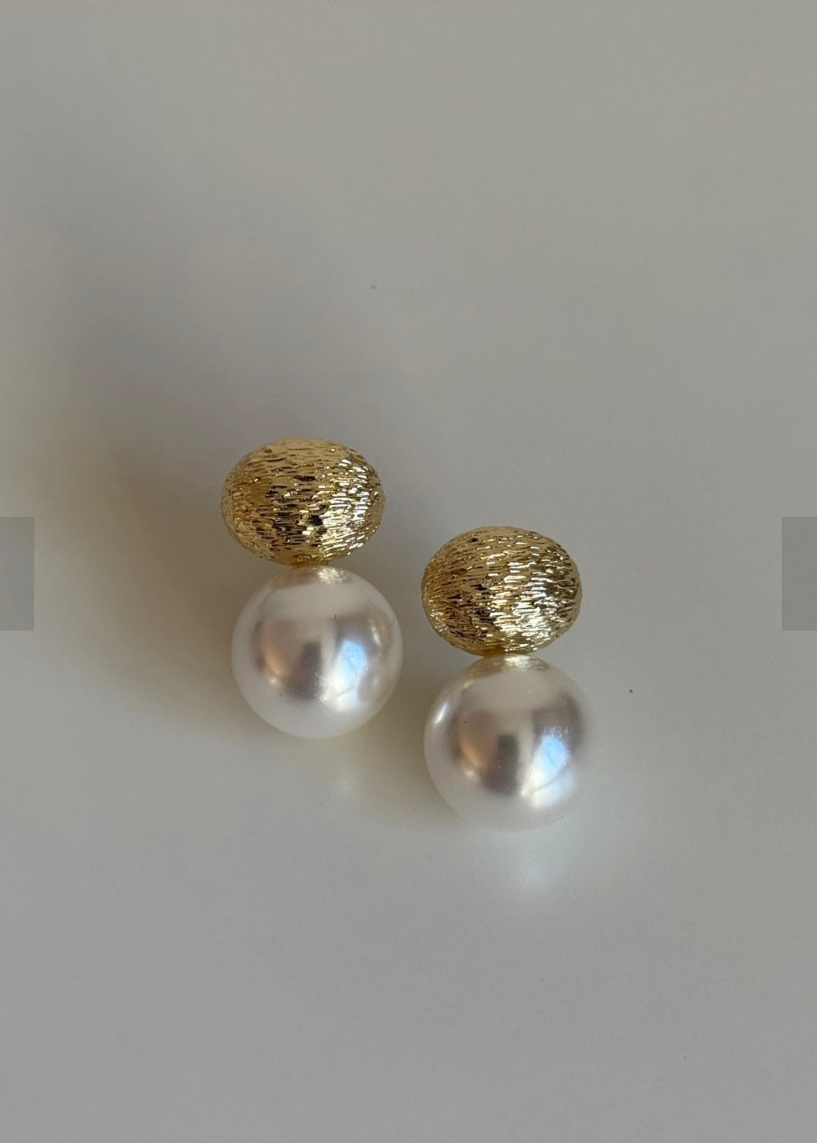 Pair of pearl earrings with gold tops on a light gray background