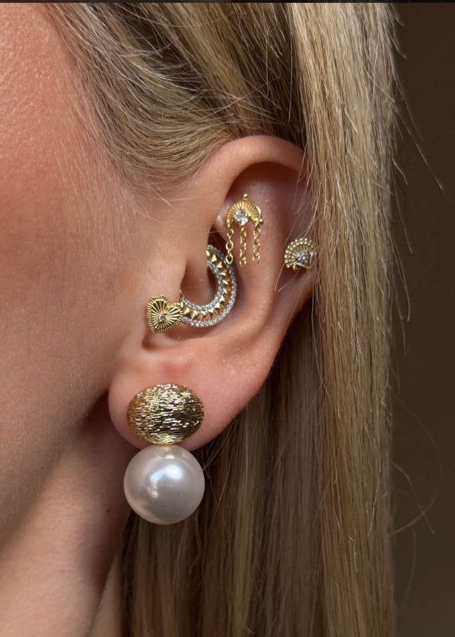 Close-up of an ear with gold and pearl earrings against a neutral background