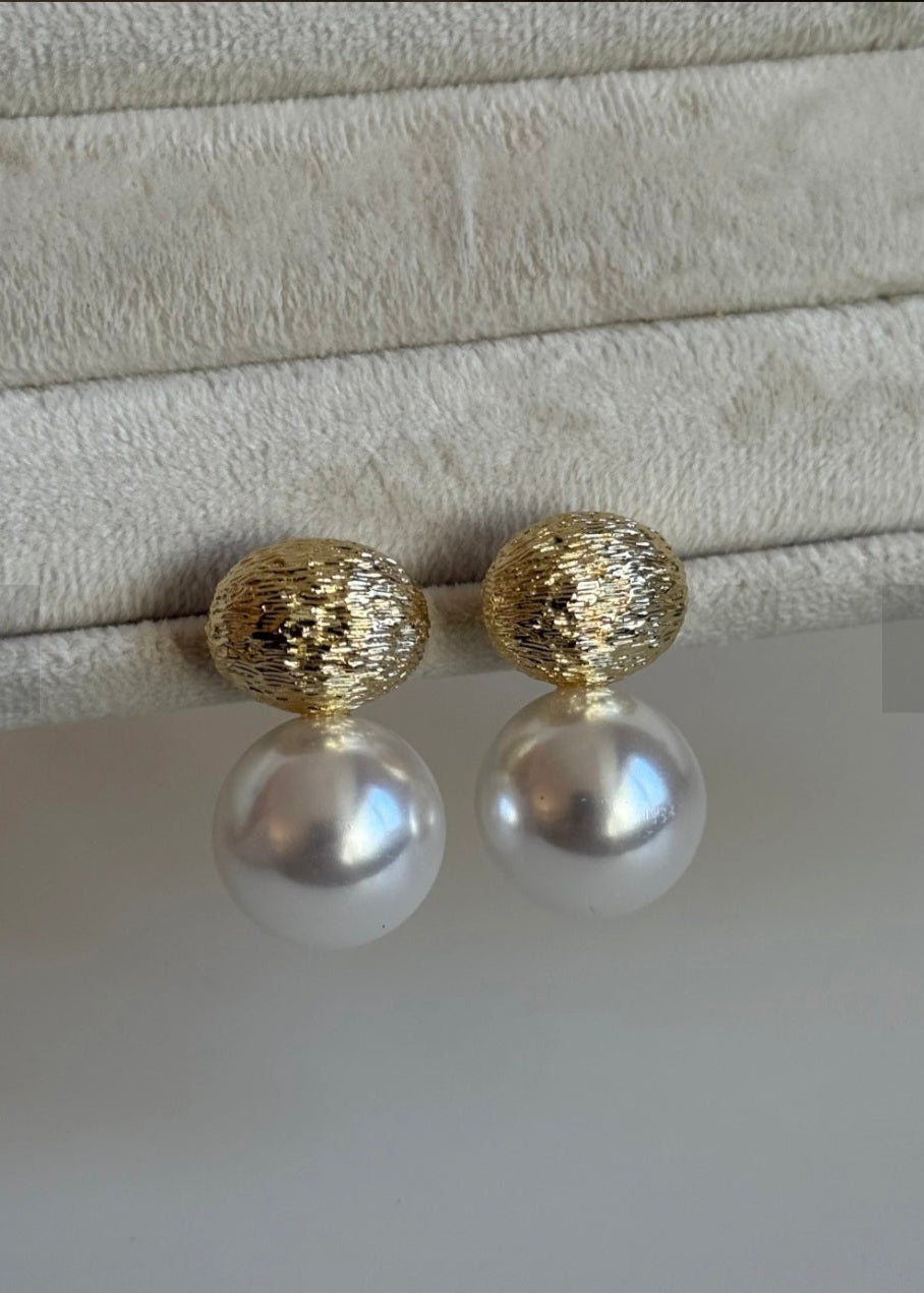 Pearl earrings with gold tops on a textured surface