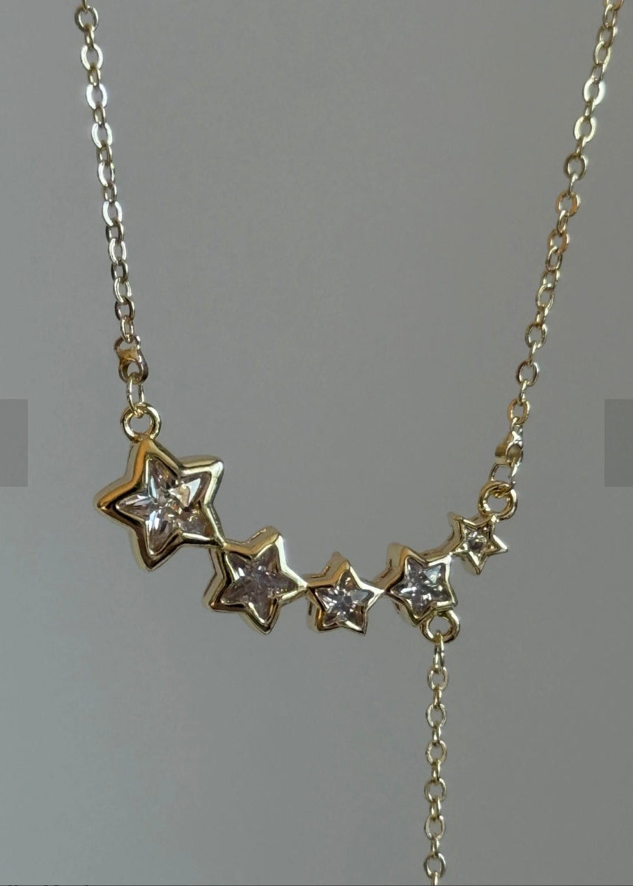 Gold necklace with star-shaped pendants on a gray background