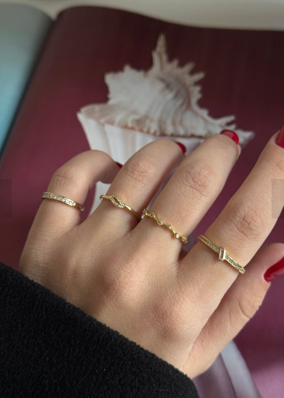 Hand wearing multiple gold rings with a shell in the background