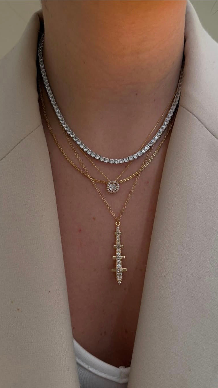 Necklace with a cross pendant worn by a person in a light-colored blazer.