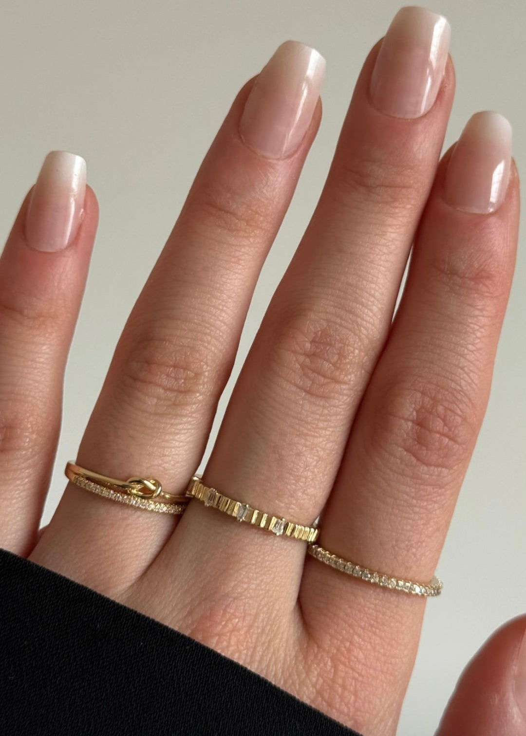 Close-up of a hand wearing two gold rings on a neutral background