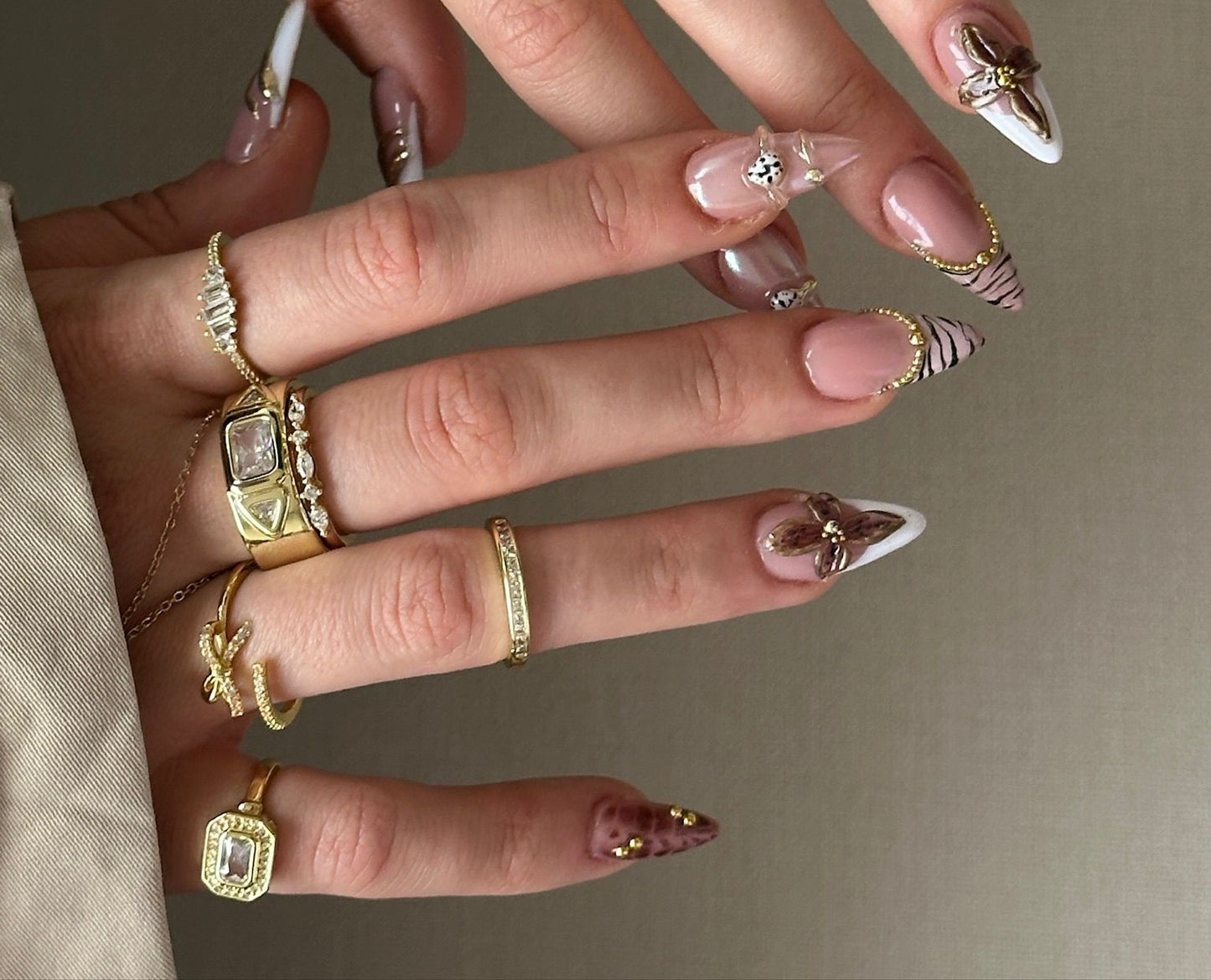 Close-up of a hand with gold rings and decorative nails on a neutral background