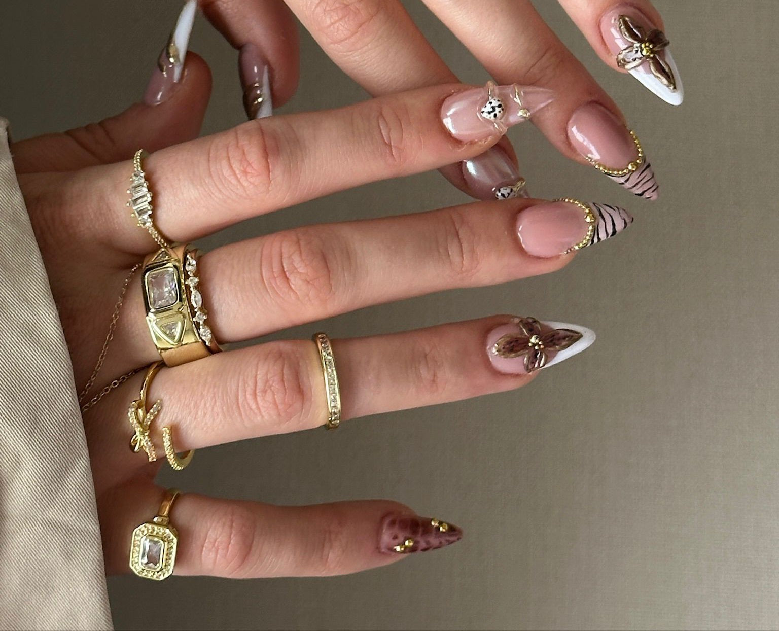 Close-up of a hand with gold rings and decorative nails on a neutral background
