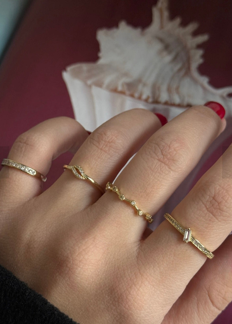 Hand wearing multiple gold rings with a shell in the background