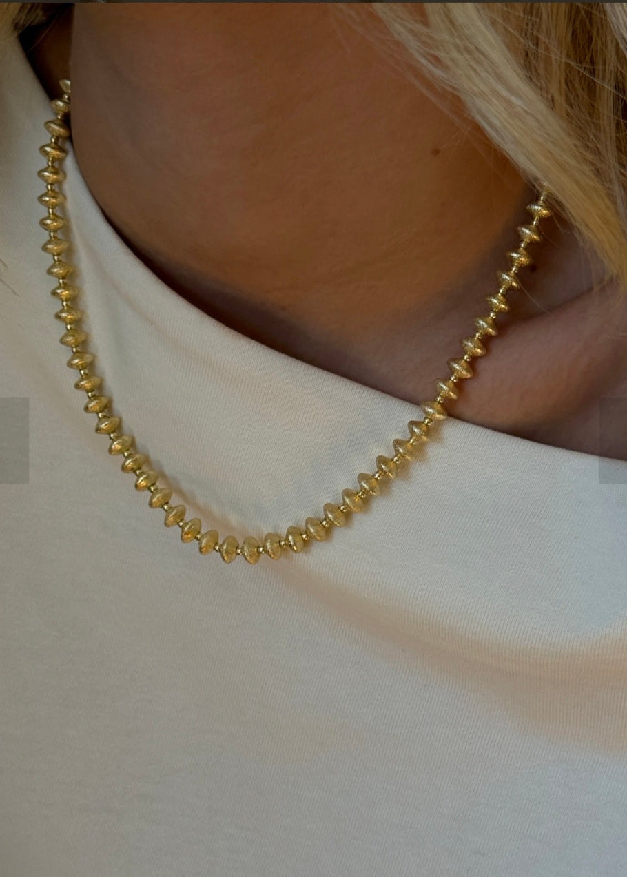Gold beaded necklace worn by a person on a plain background