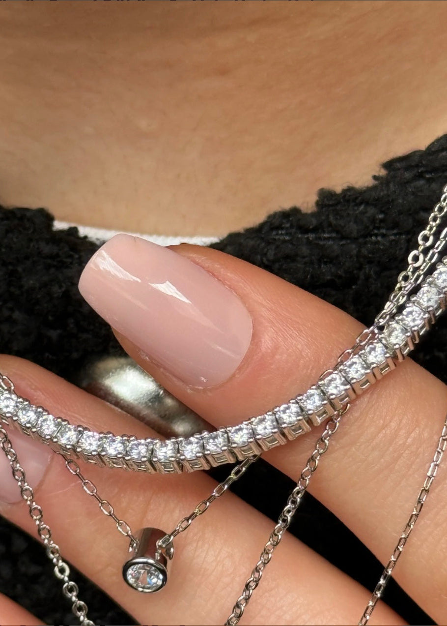 Close-up of a hand wearing multiple diamond bracelets on a neutral background