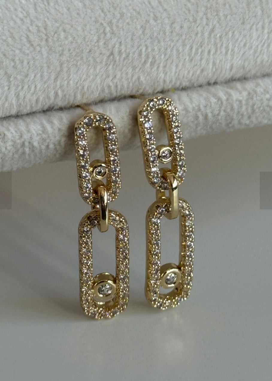 Gold chain-style earrings with small diamonds on a light gray background