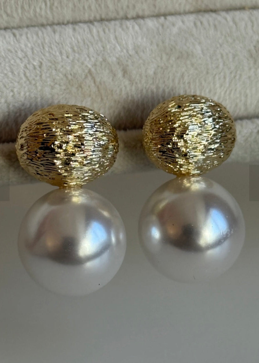 Gold and pearl earrings on a textured surface