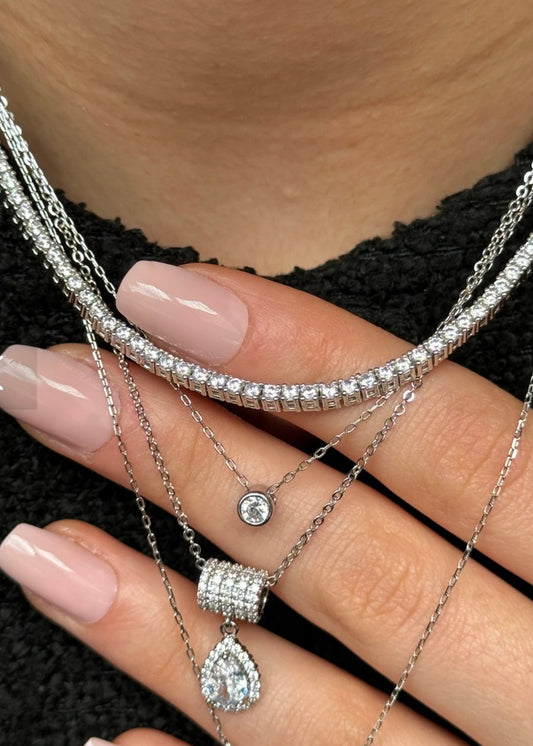 Close-up of a hand wearing multiple silver jewelry pieces on a black textured background