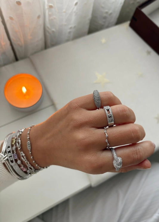 Hand wearing multiple silver rings with a candle in the background